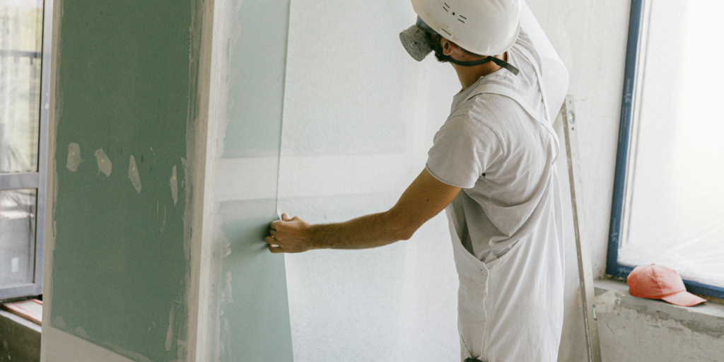 Construction worker installing green drywall sheet during drywall boarding in Abbotsford home renovation
