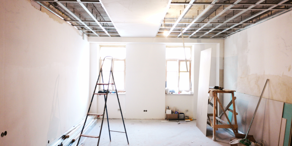 Interior renovation scene with drywall ceiling framework, ladders, and unfinished walls.

