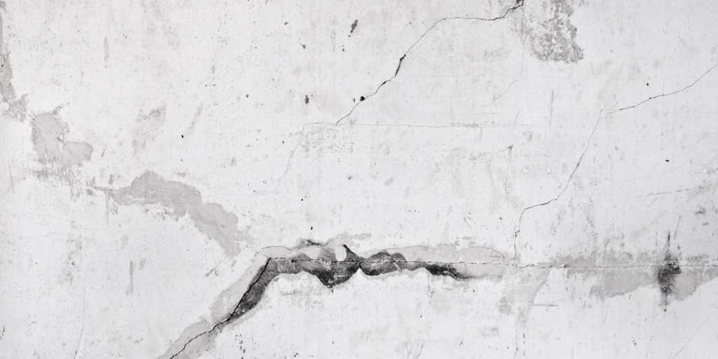 A white concrete wall with multiple long cracks and dark stains running across the surface.