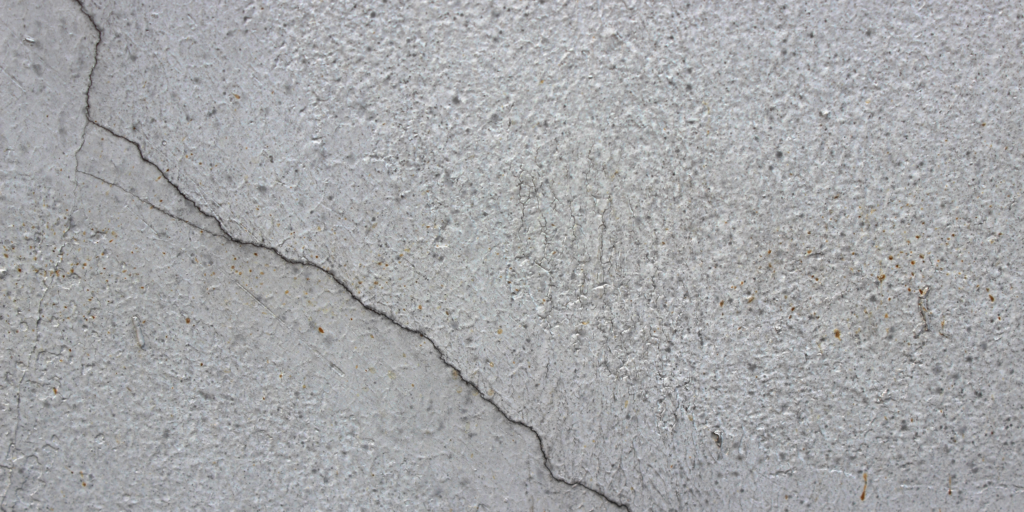 A close up view of a gray textured concrete wall with a thin jagged crack spreading across it.